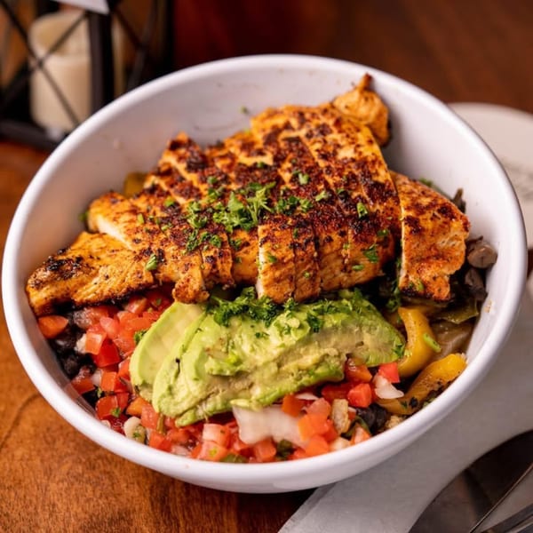 Grilled chicken breast with avocado, pico de gallo, and black beans in a white bowl.