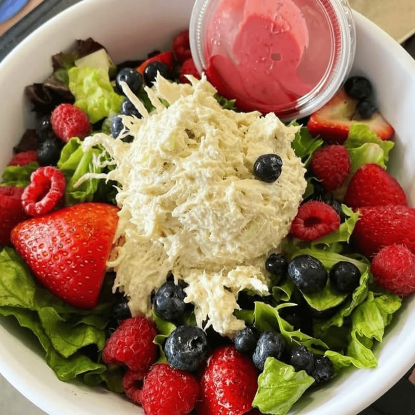 Chicken salad with mixed greens, strawberries, raspberries, blueberries, and a side of dressing.