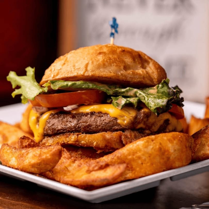 Cheeseburger with lettuce, tomato, and onions, served with a side of potato wedges.