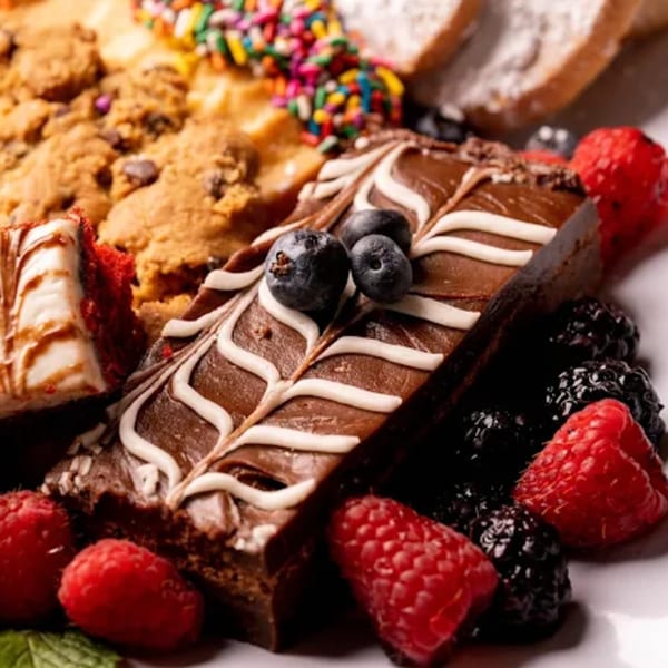 A dessert platter with chocolate brownies, cookies, red velvet cake, and fresh berries.