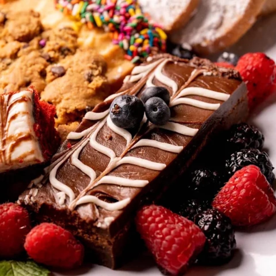 A dessert platter with chocolate brownies, cookies, red velvet cake, and fresh berries.