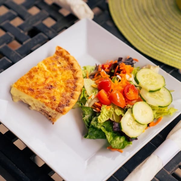 A slice of quiche and a fresh side salad with lettuce, tomatoes, cucumbers, and carrots.