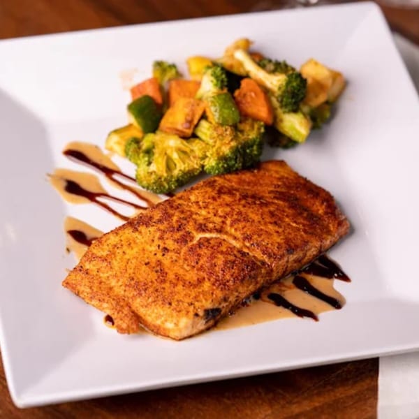 Grilled salmon with roasted broccoli and sweet potatoes, drizzled with balsamic glaze on a white plate.