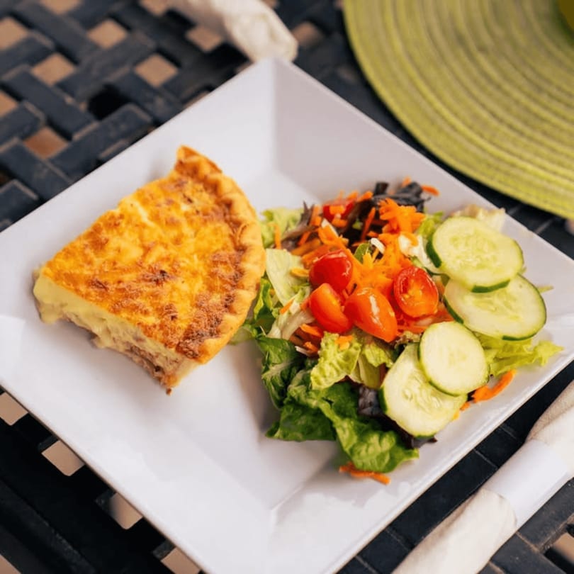 A slice of quiche and a fresh garden salad with cucumbers and tomatoes on a white plate.