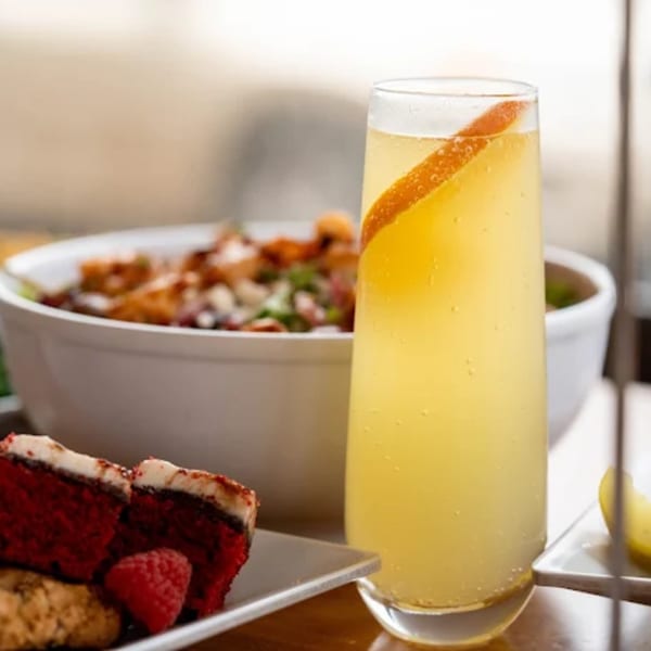 A mimosa with an orange peel garnish, red velvet cake, and a bowl of food.
