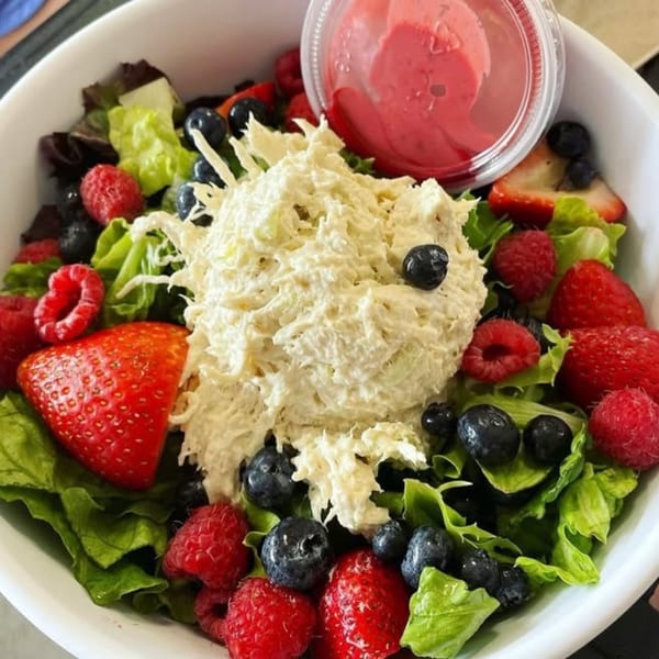 Chicken salad with mixed greens, strawberries, raspberries, blueberries, and a side of dressing.