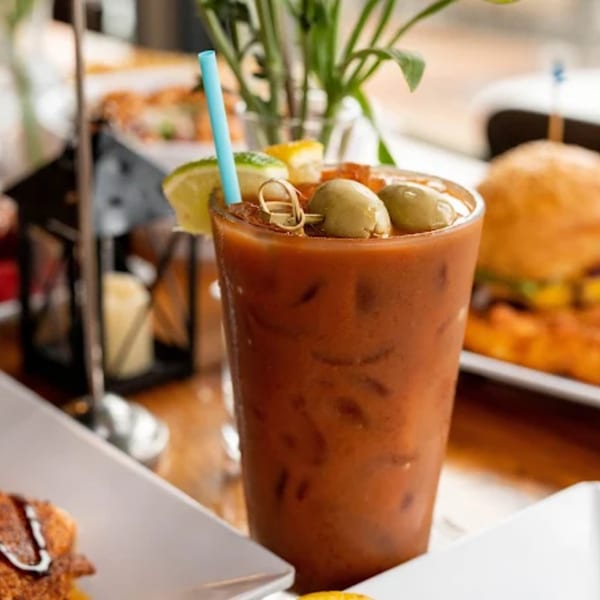 A Bloody Mary cocktail garnished with olives, lime, and lemon, with a blue straw.