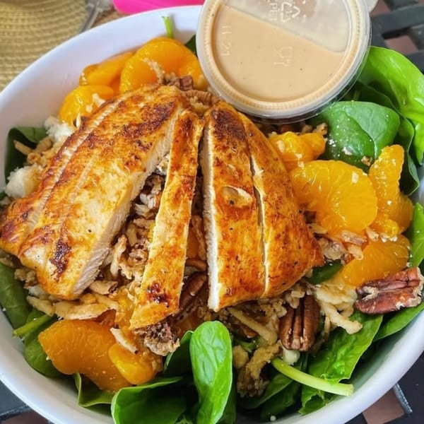 Grilled chicken salad with spinach, mandarin oranges, pecans, and crispy onions, with dressing on the side.